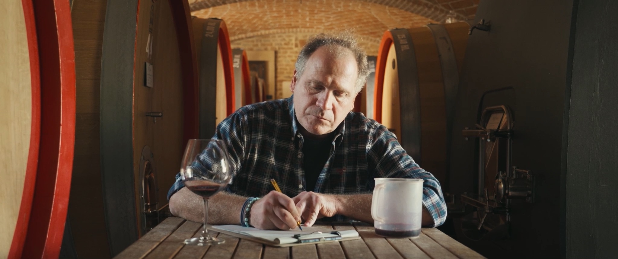 Dino, an elderly winegrower, sits alone at a table taking notes about wine.